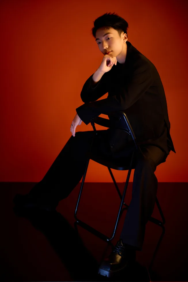 Seated black suit portrait of Z·GY against red